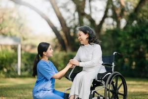 Elderly asian senior woman on wheelchair with Asian careful caregiver. Nursing home hospital garden concept. in sun light photo