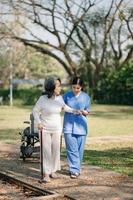 Elderly asian senior woman on wheelchair with Asian careful caregiver. Nursing home hospital garden concept. photo