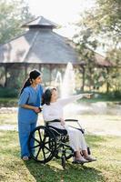 Elderly asian senior woman on wheelchair with Asian careful caregiver. Nursing home hospital garden concept. in sunlight photo