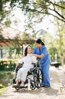 mayor asiático mayor mujer en silla de ruedas con asiático Cuidado cuidador y animar paciente, caminando en jardín. con cuidado desde un cuidador y mayor salud seguro. foto