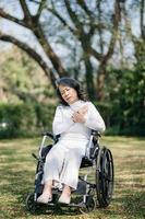 Asian old woman sitting on a wheelchair outdoors in the park Have pain in the arms, wrists and body in sun light photo