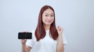 Smiling red-haired woman pointing at mobile phone isolated on white background with copy space. video