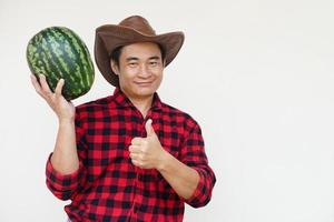 Handsome Asian man wears hat, red plaid shirt, holds watermelon fruit. Concept, Agriculture occupation, Thai farmer, grow and sell watermelon fruits as economic crop photo