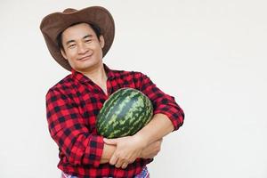 Handsome Asian man wears hat, red plaid shirt, holds watermelon fruit. Concept, Agriculture occupation, Thai farmer, grow and sell watermelon fruits as economic crop photo