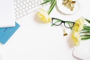 Home office clipboard desk with copy space, clipboard, pen, glasses, notepad and paper clips and tulip flowers on a white background. Flat layout, workspace layout, top view. photo