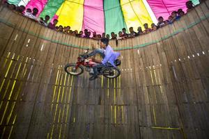 Bangladesh February 14, 2018 A rural stunt biker is risking his life by scaling the wall of a large wooden well in a motorbike carnival sideshow at Bogura, Dhaka. photo