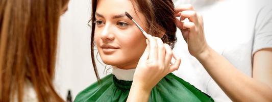 Makeup artist combing eyebrows and hairstylist preparing hairstyle photo