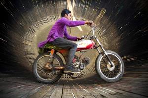 Bangladesh February 14, 2018 A rural stunt biker is risking his life by scaling the wall of a large wooden well in a motorbike carnival sideshow at Dohar, Dhaka. photo