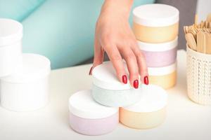 Beautician's hand takes jar with cosmetics from table offering and selling cosmetic products, moisturizing cream, wax paste. photo