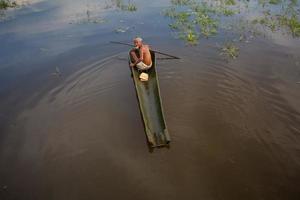 Bangladesh August 05, 2019 An old man is driving a boat made from the bark of his palm tree at Narsingdi, Bangladesh. photo