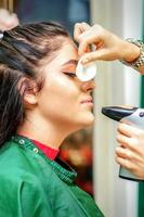 Side view of a make-up artist using aerograph making an airbrush makeup foundation on a female face in a beauty salon. photo