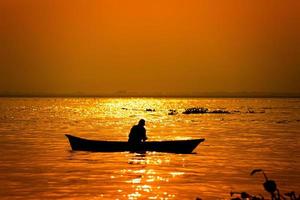 Evening golden sunset time, a fisherman fishing on the seaside on a boat. photo