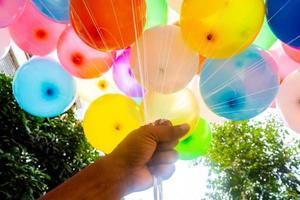 A fistful of hands is holding a bunch of colored gas-filled balloons. Colorful balloons background. photo