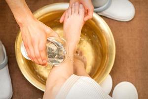 Top view of hands of masseur washing legs of a young woman in a golden bowl at beauty spa salon. photo