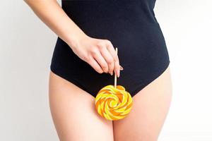 Woman holding lollipop candy on bikini zone, the concept of intimate depilation, problems of intimate hygiene. photo