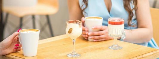 Hands of a young woman holding a cup of coffee with different cocktails on the table at the cafe. photo