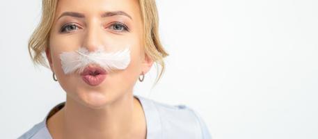 Funny beautician with a white feather-like mustache poses on white background, depilation concept. photo