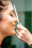 Side view of a make-up artist using aerograph making an airbrush makeup foundation on a female face in a beauty salon. photo