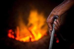 Unsafe worker hands. A local steel machine parts making yard worker melting scrap on hot furnace. photo