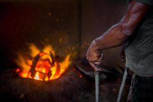 Unsafe worker hands. A local steel machine parts making yard worker melting scrap on hot furnace. photo