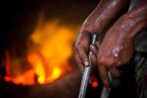 Unsafe worker hands. A local steel machine parts making yard worker melting scrap on hot furnace. photo