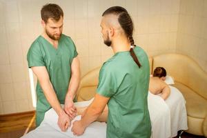 Two masseurs do foot massage in four hands for a female client in a spa salon. photo