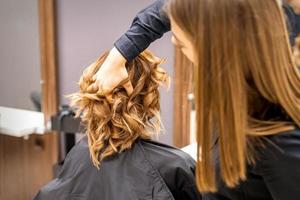 Female hairdresser checks brown curly hairstyle of a young caucasian woman in beauty salon. photo