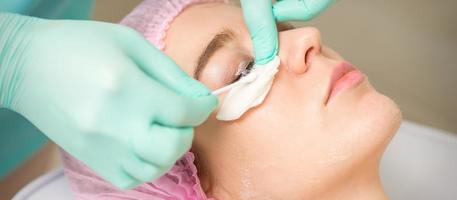 Young woman receiving eyelash removal procedure and removes mascara with a cotton swab and stick in a beauty salon. photo