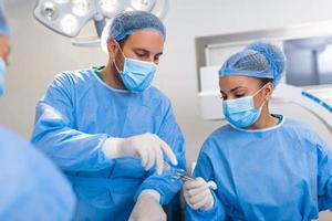 Low Angle Shot in the Operating Room, Assistant Hands out Instruments to Surgeons During Operation. Surgeons Perform Operation. Professional Medical Doctors Performing Surgery. photo