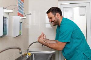 Doctor washing hands with soap. Male surgeon is preparing for surgery. He is in uniform at operating room. photo