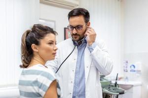 Young doctor is using a stethoscope listen to the heartbeat of the patient. Shot of a male doctor giving a female patient a check up photo