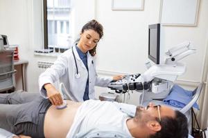 Young male patient lying on bed and having ultrasound examination of abdomen in medical clinic photo