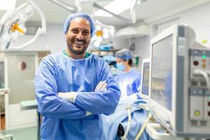 Anesthetist Working In Operating Theatre Wearing Protecive Gear checking monitors while sedating patient before surgical procedure in hospital photo