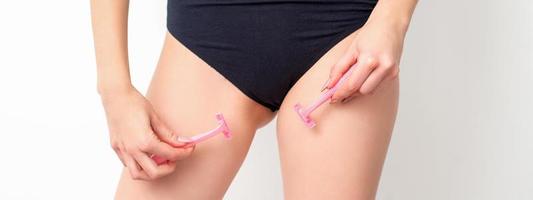 Young woman shaving crotch in bikini zone with two razors standing on white background, concept skincare and hair removal. photo