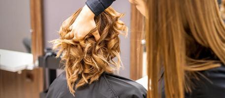 Female hairdresser checks brown curly hairstyle of a young caucasian woman in beauty salon. photo