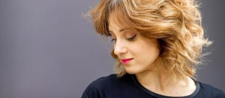 Beautiful young caucasian woman with a red short curly hairstyle looking down on dark background. photo