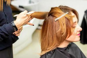 el hembra cliente recepción un Corte de pelo a el belleza salón, joven mujer disfrutando consiguiendo un nuevo peinado. foto