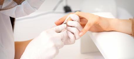 Close up of manicure master with manicure nipper cuts cuticles of female nails at beauty salon. photo