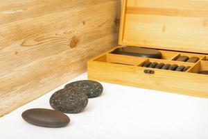 Black massage stones lying near the wooden box with massage rocks on the towel on the table. photo