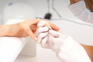 Close up of manicure master with manicure nipper cuts cuticles of female nails at beauty salon. photo