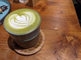 Close up green matcha latte over the wooden table on the cafe and resto. The photo is suitable to use for coffee shop background, menu poster and matcha content media.