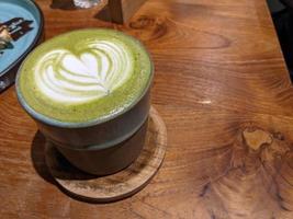 Close up green matcha latte over the wooden table on the cafe and resto. The photo is suitable to use for coffee shop background, menu poster and matcha content media.