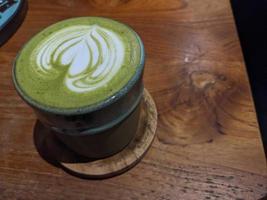 Close up green matcha latte over the wooden table on the cafe and resto. The photo is suitable to use for coffee shop background, menu poster and matcha content media.