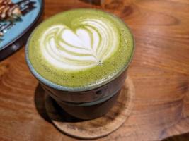 Close up green matcha latte over the wooden table on the cafe and resto. The photo is suitable to use for coffee shop background, menu poster and matcha content media.