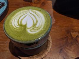 Close up green matcha latte over the wooden table on the cafe and resto. The photo is suitable to use for coffee shop background, menu poster and matcha content media.