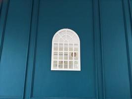 Window mirror on the center of blue background wall. The photo is suitable to use for abstract background and interior content media.