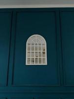 Window mirror on the center of blue background wall. The photo is suitable to use for abstract background and interior content media.