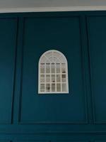 Window mirror on the center of blue background wall. The photo is suitable to use for abstract background and interior content media.