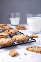 Baked oatmeal cookies with chocolate chips on a metal cooling rack and milk in a glass. photo