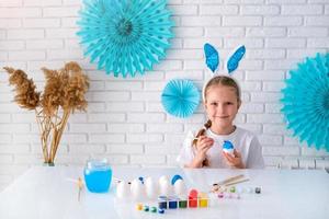 Little girl painting eggs with blue paint. Happy Easter.  Child making easter decoration at home. photo